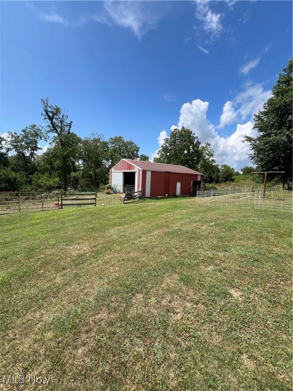 view of yard with a garage, a rural view, a pole building, and an outbuilding