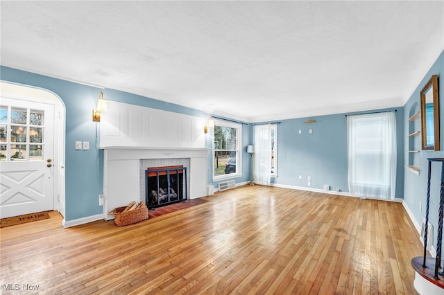 unfurnished living room with a brick fireplace, wood-type flooring, visible vents, and baseboards