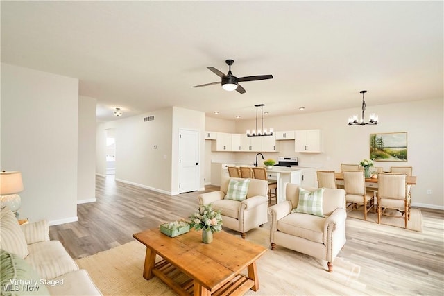 living room featuring light wood-type flooring, baseboards, visible vents, and ceiling fan with notable chandelier