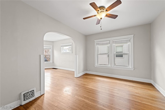 unfurnished room with arched walkways, light wood-style flooring, a ceiling fan, visible vents, and baseboards