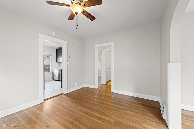 spare room with light wood-style floors, baseboards, arched walkways, and a ceiling fan