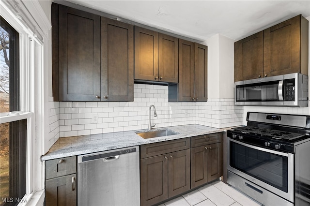 kitchen featuring light tile patterned floors, tasteful backsplash, light stone counters, stainless steel appliances, and a sink