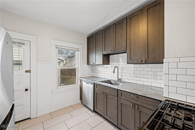 kitchen featuring a wainscoted wall, dark brown cabinetry, a sink, light stone countertops, and dishwasher