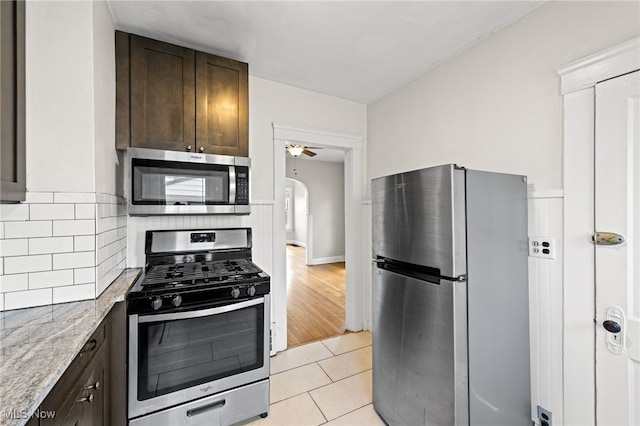 kitchen featuring tasteful backsplash, appliances with stainless steel finishes, light stone counters, dark brown cabinets, and light tile patterned flooring