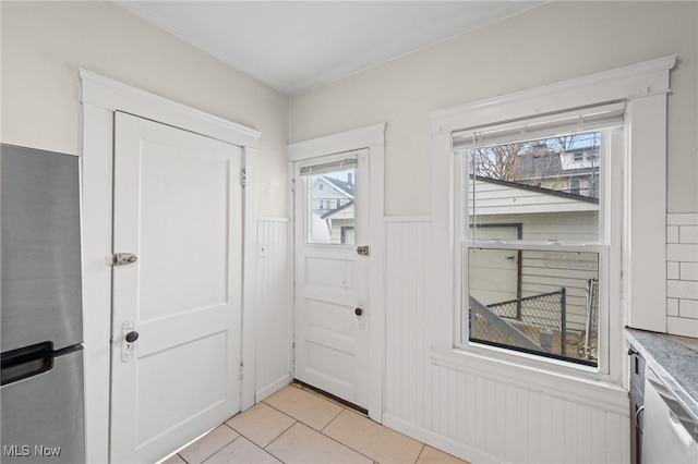 doorway with a wainscoted wall and light tile patterned flooring