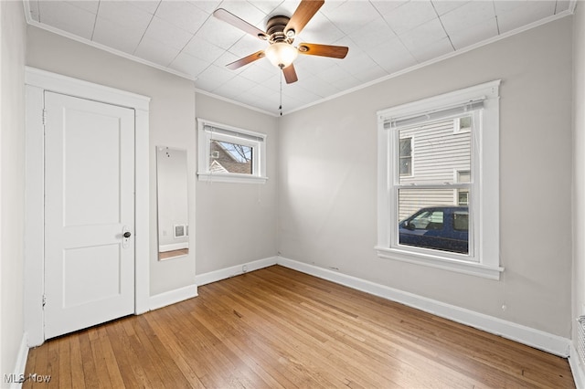 empty room featuring a ceiling fan, baseboards, crown molding, and light wood finished floors