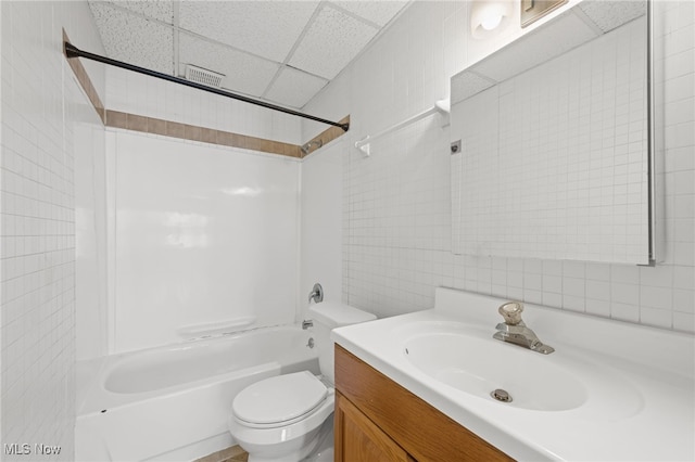 full bath featuring toilet, shower / bathtub combination, vanity, a paneled ceiling, and tile walls