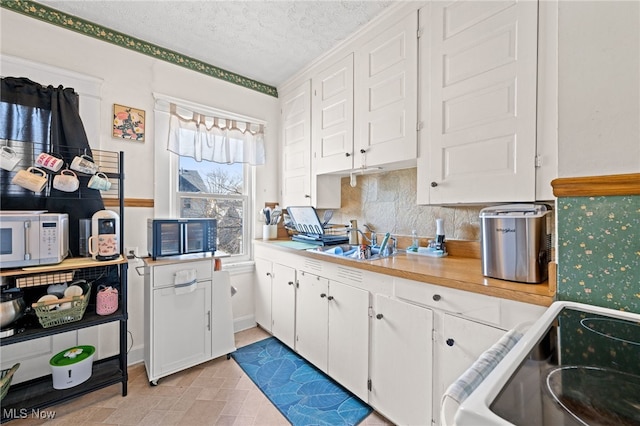 kitchen featuring white cabinets, white microwave, stove, light countertops, and a sink