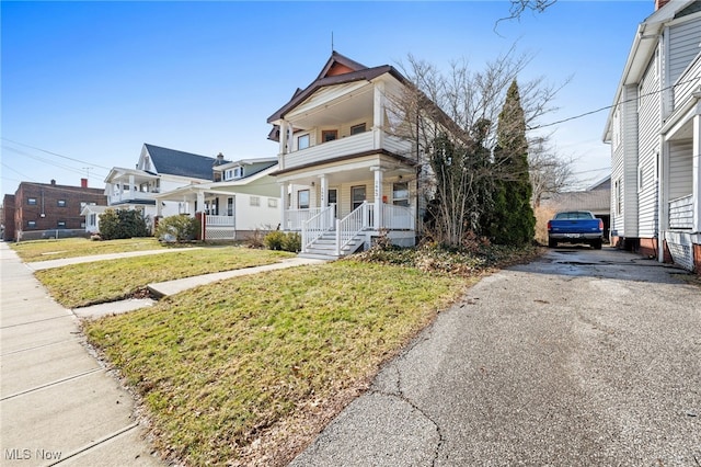 view of front facade with driveway, a balcony, a front lawn, and a porch