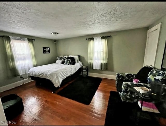 bedroom with multiple windows, wood finished floors, and baseboards