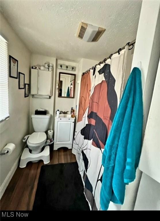 full bath featuring curtained shower, visible vents, toilet, a textured ceiling, and wood finished floors