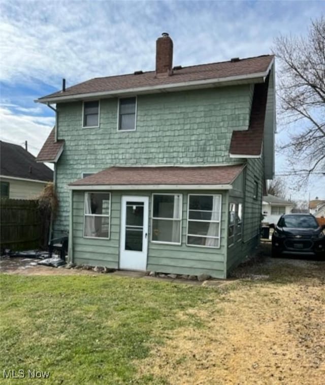 back of property with a chimney, fence, and a lawn