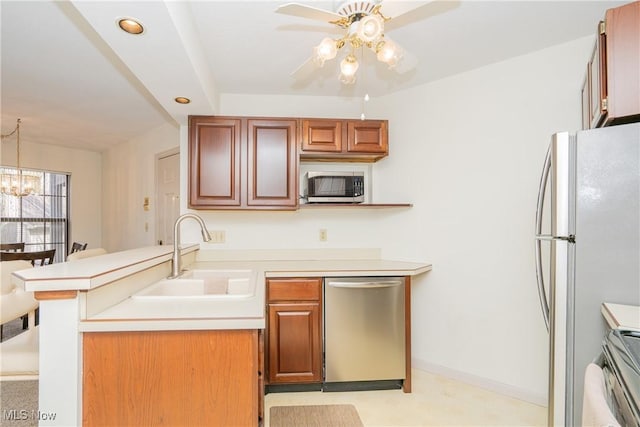 kitchen featuring appliances with stainless steel finishes, a peninsula, light countertops, a sink, and ceiling fan with notable chandelier