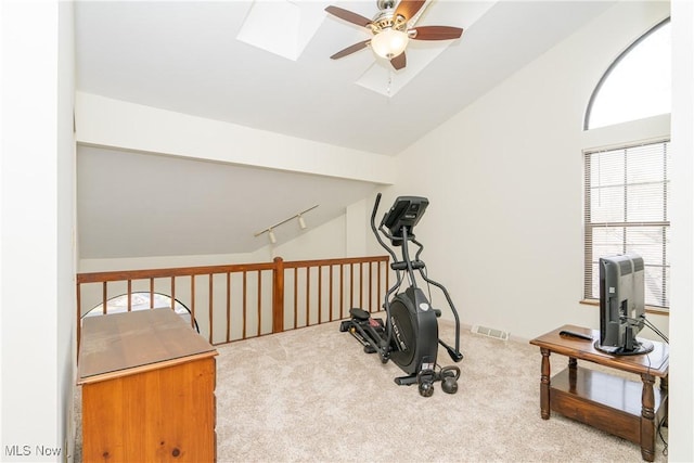 exercise room featuring vaulted ceiling with skylight, visible vents, a ceiling fan, carpet, and track lighting