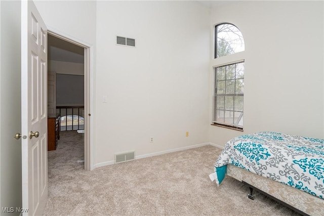 carpeted bedroom with visible vents, a towering ceiling, and baseboards