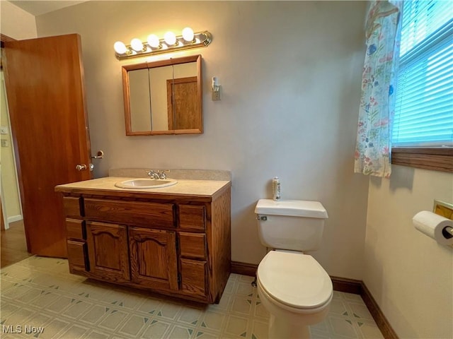 half bath with toilet, tile patterned floors, baseboards, and vanity