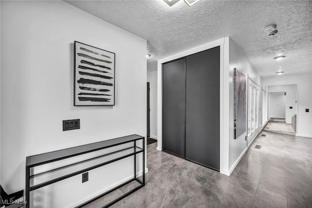 hallway with a textured ceiling, visible vents, and baseboards