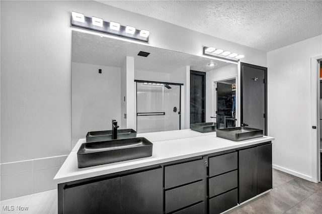 bathroom with double vanity, a textured ceiling, a shower, and a sink