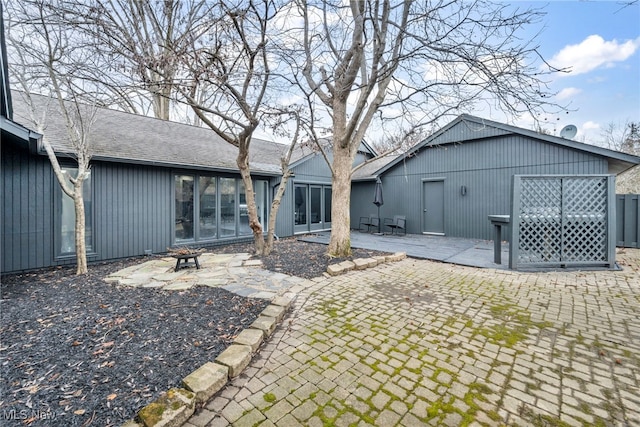 rear view of house with an outdoor fire pit, a patio area, and roof with shingles