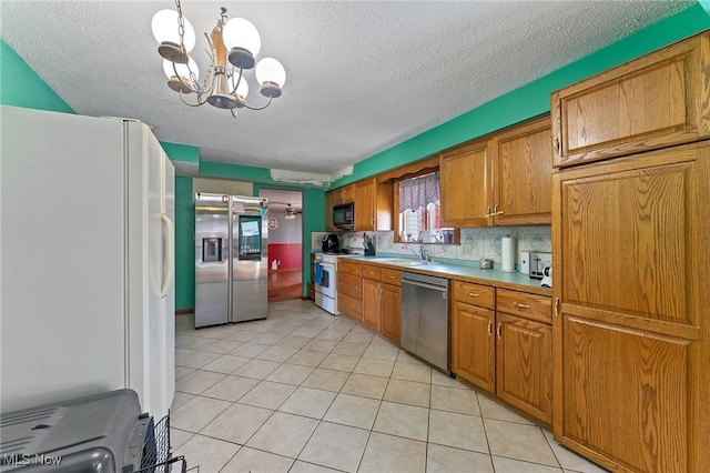 kitchen with brown cabinets, an inviting chandelier, appliances with stainless steel finishes, light tile patterned flooring, and a sink