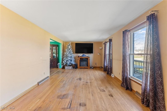 unfurnished living room featuring light wood-style floors, baseboards, visible vents, and a glass covered fireplace