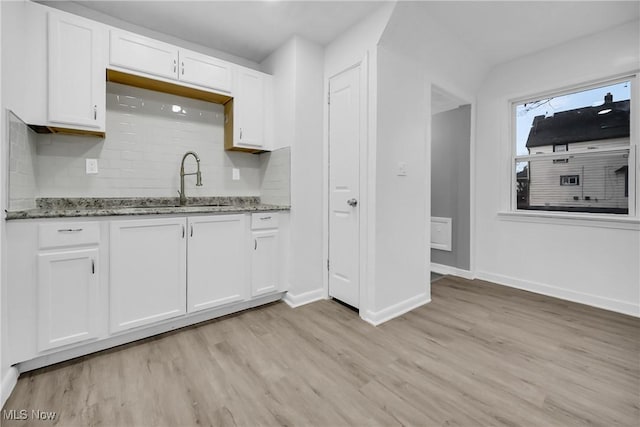 kitchen with light wood finished floors, tasteful backsplash, white cabinets, stone counters, and a sink