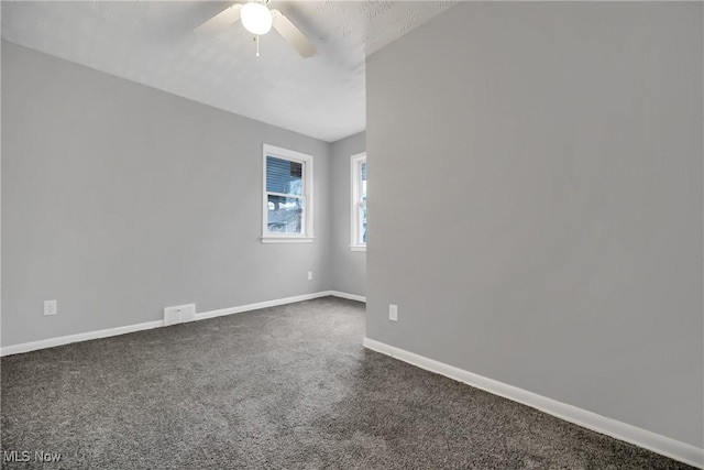 empty room featuring visible vents, dark carpet, baseboards, and ceiling fan