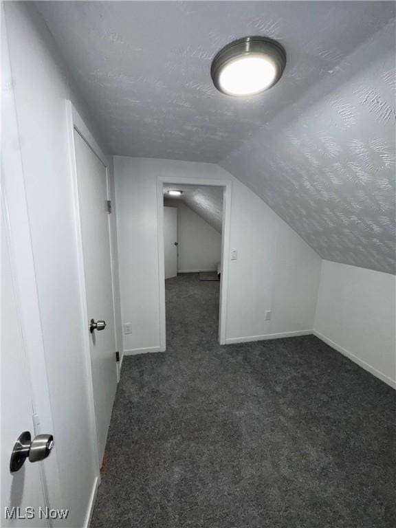 bonus room with a textured ceiling, vaulted ceiling, dark carpet, and baseboards