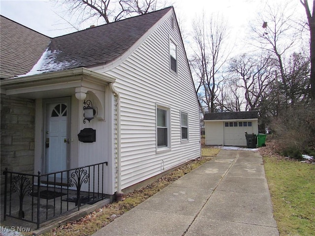 view of side of home featuring roof with shingles, an outdoor structure, and a detached garage