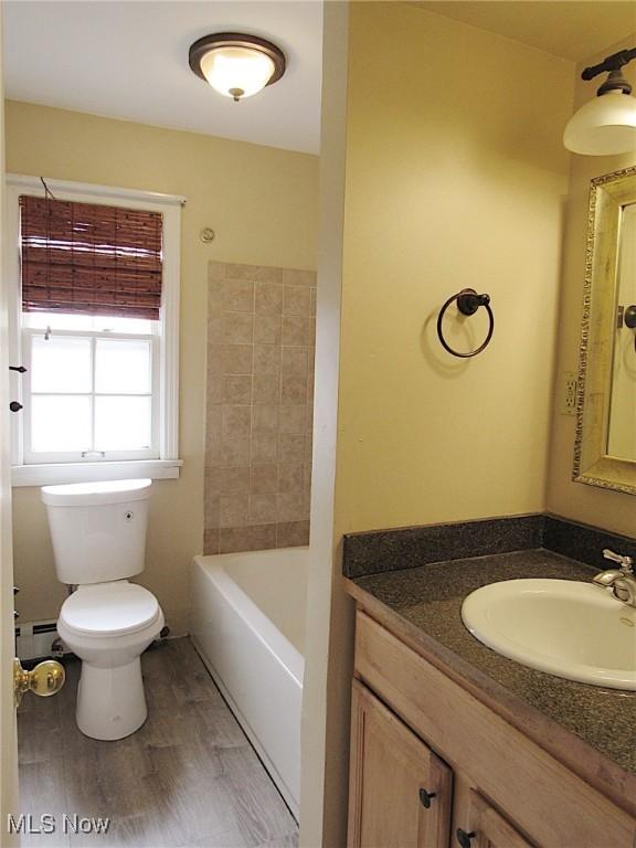 full bath with a baseboard radiator, a bathing tub, toilet, wood finished floors, and vanity