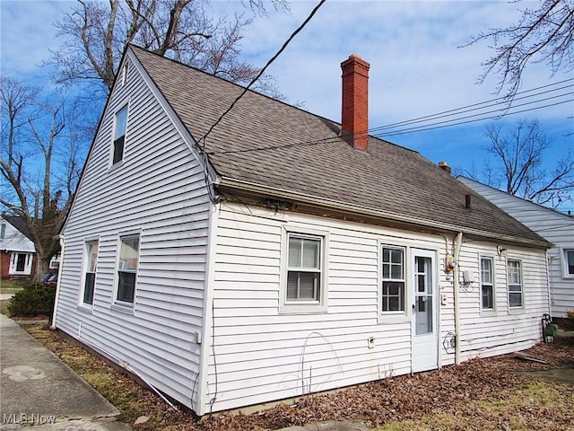 back of house with a chimney and roof with shingles