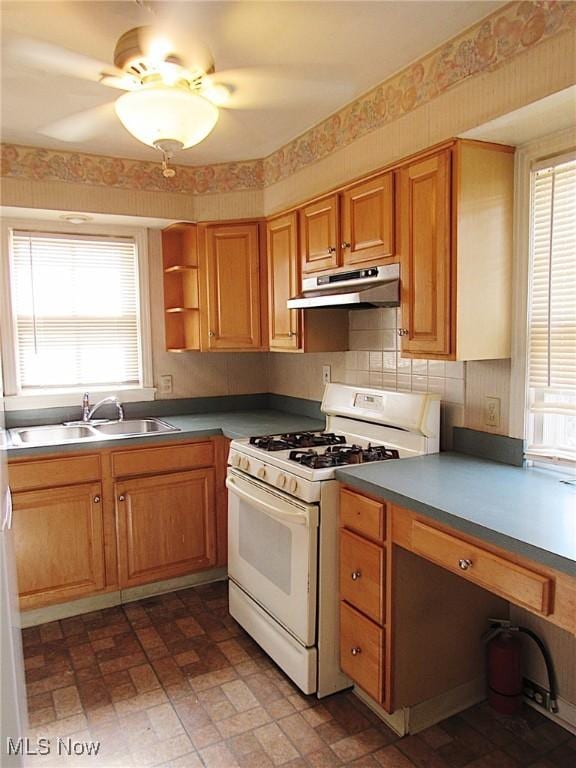 kitchen featuring white gas stove, a healthy amount of sunlight, a sink, and under cabinet range hood