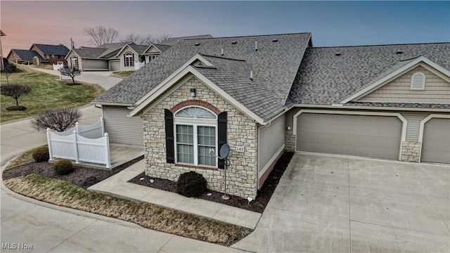 view of front of house with stone siding, concrete driveway, roof with shingles, and an attached garage