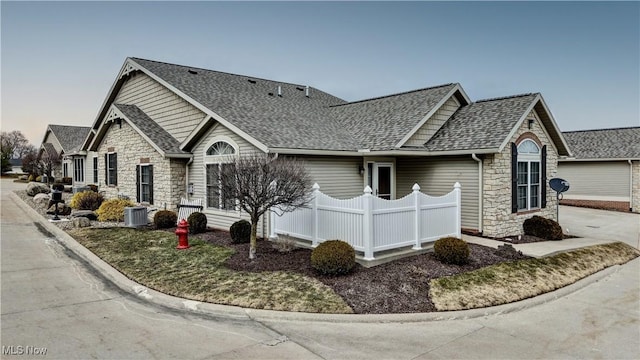 view of front of home with central air condition unit, stone siding, and roof with shingles