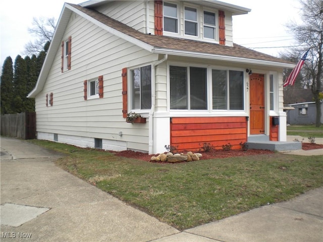 bungalow-style home featuring a shingled roof, fence, and a front yard