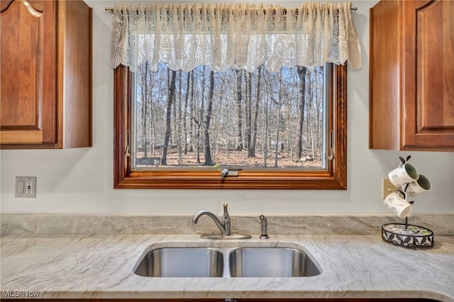 kitchen with brown cabinets, plenty of natural light, a sink, and light stone countertops