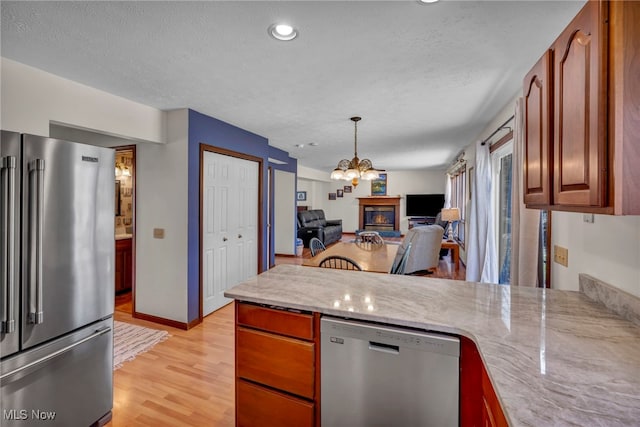 kitchen featuring light wood-style flooring, stainless steel appliances, a peninsula, open floor plan, and a glass covered fireplace