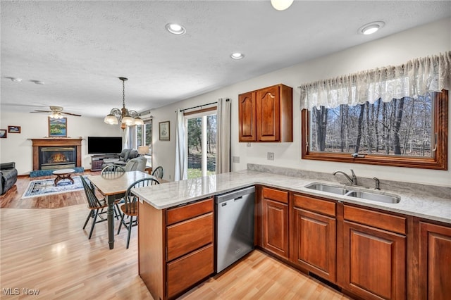 kitchen featuring light wood-style floors, a glass covered fireplace, a sink, dishwasher, and a peninsula