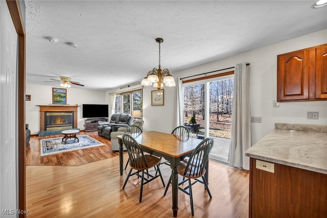 dining area with light wood-style floors, ceiling fan with notable chandelier, a textured ceiling, and a glass covered fireplace