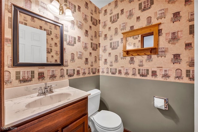 bathroom featuring vanity, toilet, and wallpapered walls