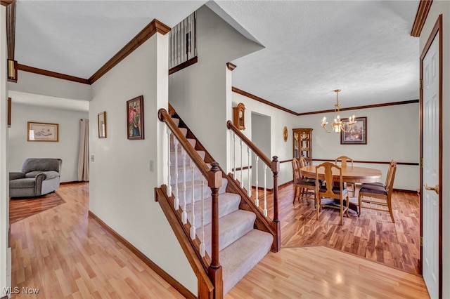 stairway with baseboards, wood finished floors, crown molding, a textured ceiling, and a chandelier