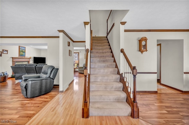 stairway with crown molding, a fireplace, baseboards, and wood finished floors