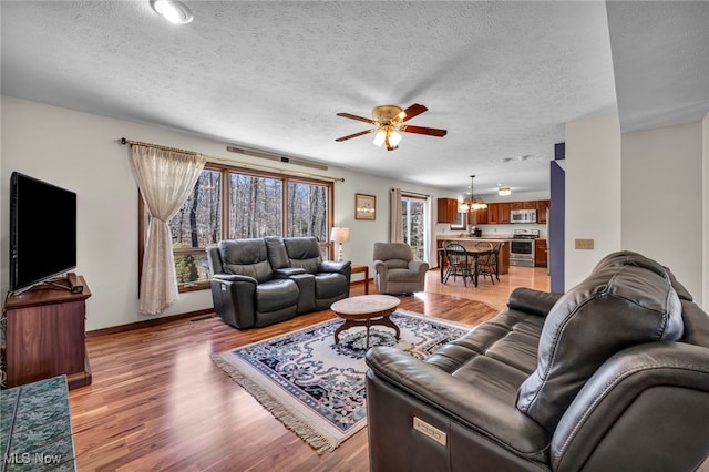 living area featuring ceiling fan with notable chandelier, light wood finished floors, a textured ceiling, and baseboards