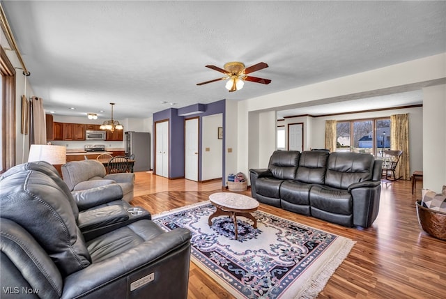 living room with light wood-type flooring, a textured ceiling, and ceiling fan with notable chandelier