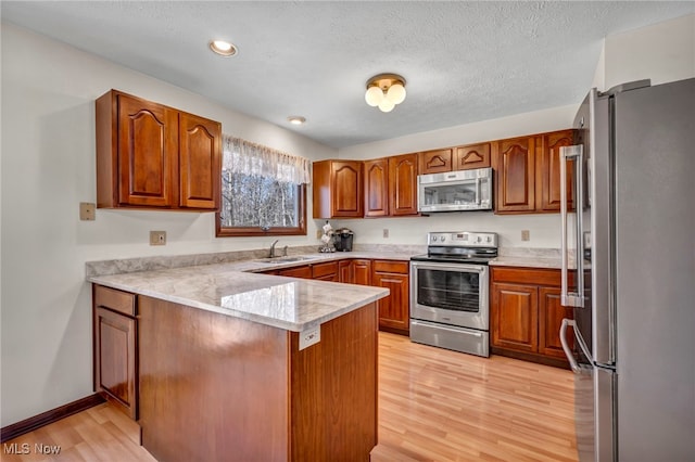 kitchen with brown cabinets, stainless steel appliances, a sink, light wood-type flooring, and a peninsula