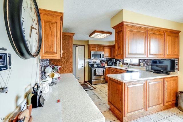 kitchen with stainless steel appliances, backsplash, a peninsula, and light countertops