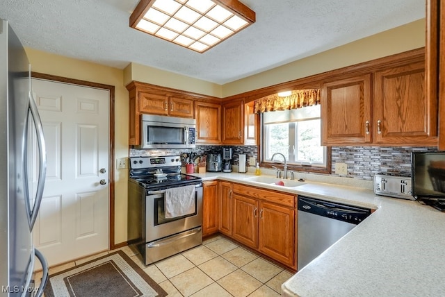 kitchen featuring brown cabinetry, appliances with stainless steel finishes, light countertops, and a sink