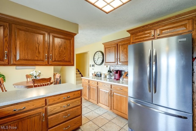 kitchen featuring light tile patterned floors, light countertops, freestanding refrigerator, and brown cabinets