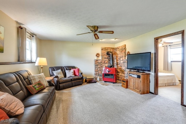 carpeted living room with a ceiling fan, a wood stove, plenty of natural light, and a textured ceiling