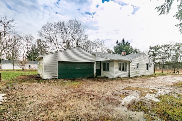 view of front of home with an attached garage, dirt driveway, and a chimney